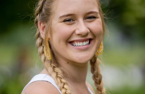 Headshot of Briella Hirsch smiling, wearing Dutch braided pigtails, 白色背心, and lemon wedge ear rings.